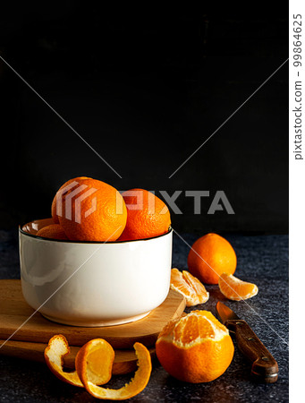 Sweet juicy tangerines in a white bowl and a knife on dark background 99864625