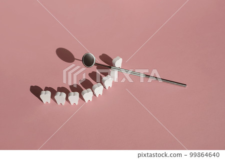Dental mirror is a tool for examining teeth and oral cavity. Models of snow-white teeth standing hardly on a pink background. View from above. World Dentist Day Dental mirror is a tool for examining teeth and oral cavity. Models of snow-white teeth standing hardly on a pink background. View from above. World Dentist Day 99864640