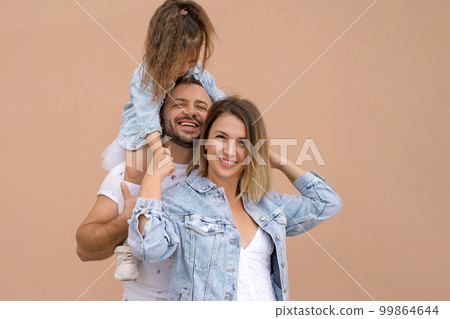 A happy young family with a small child laughs sincerely. A curly-haired girl sits on her father's shoulders. World Family Day 99864644