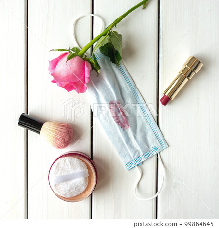Top view arrangement with make-up, rose, medical mask with lipstick trace on white wooden background Top view arrangement with make-up, rose, medical mask with lipstick trace on white wooden background 99864645