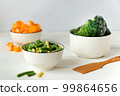 Frozen vegetables assortment. Frozen broccoli, French beans and pumpkin in white bowls on white table 99864656