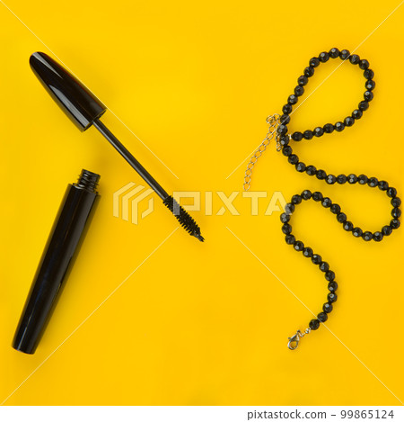 Black mascara and beads against a bright yellow background. Black mascara and beads against a bright yellow background. 99865124