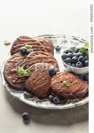 Chocolate pancakes with fresh blueberries, syrup and mint leaves in morning light close up. Healthy breakfast Chocolate pancakes with fresh blueberries, syrup and mint leaves in morning light close up. Healthy breakfast 99865800