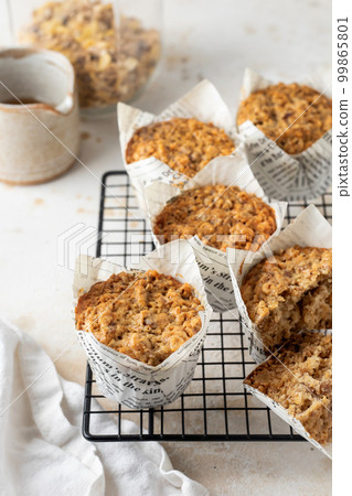 Morning breakfast oatmeal muffins in white paper cups on cooling rack on white textured background 99865801