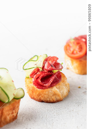 Bruschetta with sausage and vegetables on light gray background. Three of salami sandwiches as appetizer isolated with text space close up 99865809