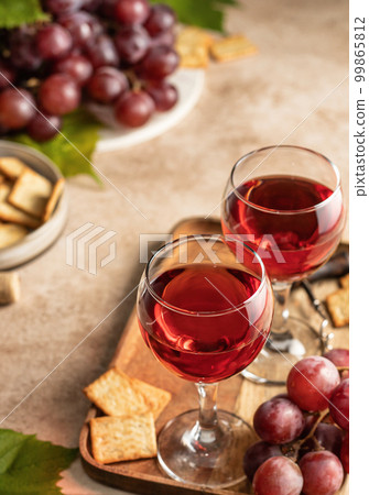 Two glasses of red wine, a bunch of red grapes, crackers and corkscrew on a wooden tray on beige textured background. Celebration party for two concept Two glasses of red wine, a bunch of red grapes, crackers and corkscrew on a wooden tray on beige textured background. Celebration party for two concept 99865812