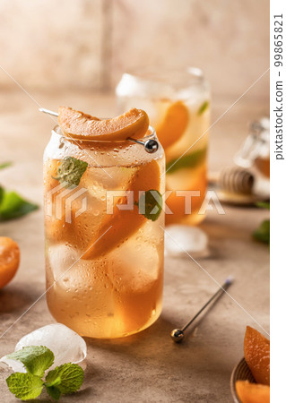 Fresh apricot cocktail, fizz or ice tea with mint and garnish. Pink beige tile background 99865821