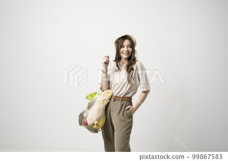 Zero waste concept. Young brunette woman holding reusable eco bag and shopping in zero waste plastic free store with reusable mesh bag. Low waste lifestyle. Sustainable eco lifestyle concept. 99867583