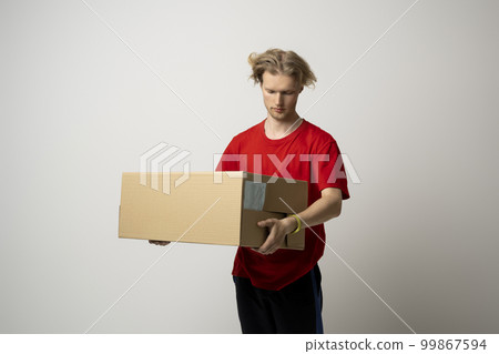 Delivery man in red uniform carry cardboard box in hands on white background. Delivery guy give parcel shipment. 99867594