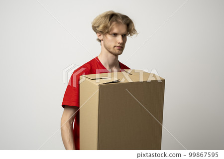 Delivery service. Happy young delivery man in red t-shirt standing with parcel isolated on white background. 99867595