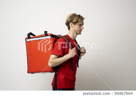 Handsome young delivery man posing with thermo backpack delivery food to client on white background. Courier male. 99867604