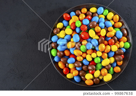 Multi-colored round candies in colored glaze in large quantities in a plate Multi-colored round candies in colored glaze in large quantities in a plate 99867638