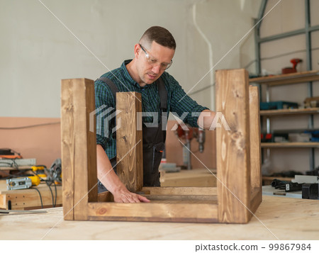 Male carpenter finishing work on wooden table in workshop. Male carpenter finishing work on wooden table in workshop. 99867984