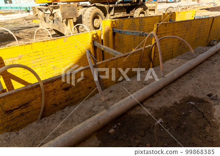 Excavator filling deep excavation supported by trench box with pipe bedding pea gravel during installation of drainage pipe. 99868385