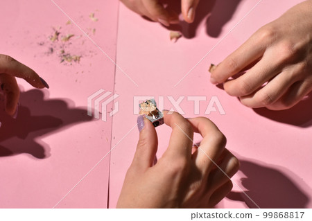 Hand holding pencil sharpener and pencil shavings on pink background. 99868817