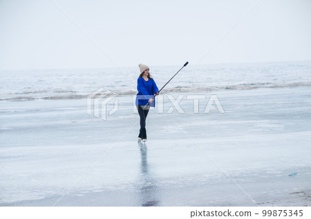 A caucasian woman is skating on a frozen lake holding a selfie stick in her hands. The figure skater films her skating. 99875345
