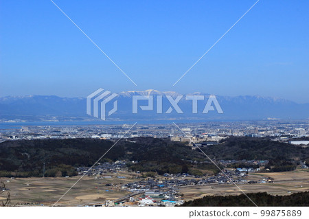 The snow-capped Hira Mountains on the opposite shore of Lake Biwa seen from the mountain trail of Doyama in the Konan Alps 99875889