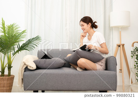 Young asian woman looking data on tablet and writing new idea of project in notebook while wearing casual Young asian woman looking data on tablet and writing new idea of project in notebook while wearing casual 99880321
