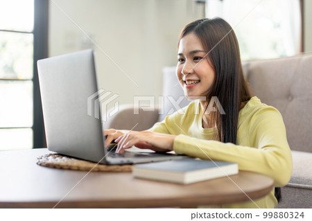 Young woman is sitting to smiling on the floor and using laptop to typing business report while working 99880324