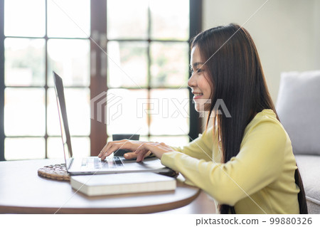 Young woman is sitting to smiling on the floor and using laptop to typing business report while working Young woman is sitting to smiling on the floor and using laptop to typing business report while working 99880326