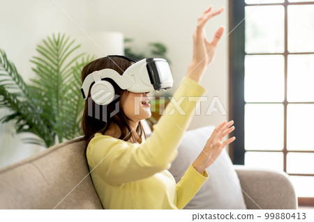 Young asian woman wearing virtual reality goggles to watching video and playing games with virtual experience Young asian woman wearing virtual reality goggles to watching video and playing games with virtual experience 99880413