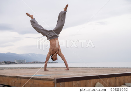 Shirtless caucasian man doing acrobatic wheel on the beach.  99881962