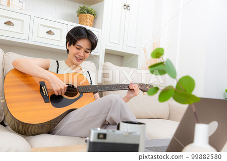 Woman playing acoustic guitar music instrument at home. 99882580