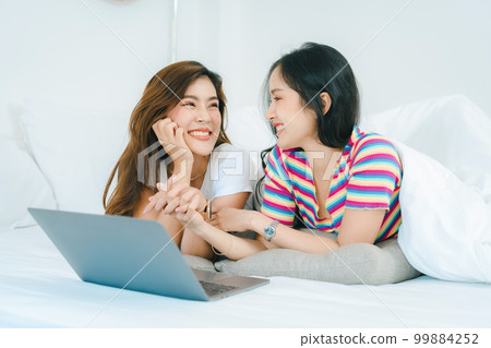 lgbtq, lgbt concept, homosexuality, portrait of two asian women posing happy together and loving each other while playing computer laptop on bed. lgbtq, lgbt concept, homosexuality, portrait of two asian women posing happy together and loving each other while playing computer laptop on bed. 99884252