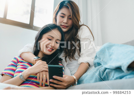 lgbtq, lgbt concept, homosexuality, portrait of two asian women enjoying together and showing love for each other while using smartphone mobile to take selfies. 99884253
