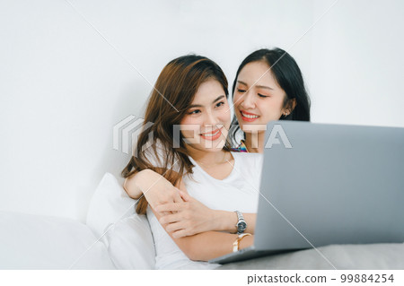 lgbtq, lgbt concept, homosexuality, portrait of two asian women posing happy together and loving each other while playing computer laptop on bed. 99884254