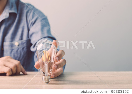 Man holding a clear light bulb on his desk with gray space wall background. Concept of new ideas at work Man holding a clear light bulb on his desk with gray space wall background. Concept of new ideas at work 99885162