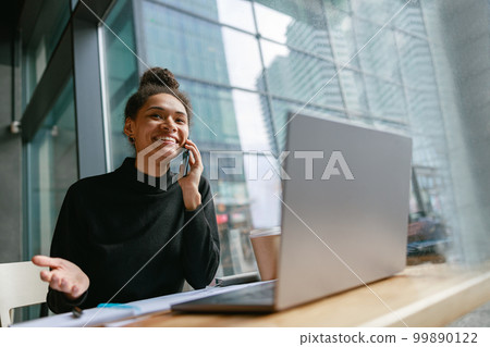 Smiling woman talking on phone with client sitting in cafe near window. Distance work concept 99890122