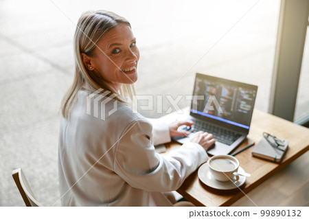 Business lady working on laptop and drinking coffee while sitting in cafe near window. Distance work 99890132
