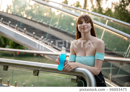 A smiling brunette in a blue T-shirt standing on the bridge. 99893475
