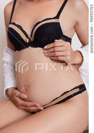 Portrait of a pregnant woman wearing black underwear, faceless shot of expectant mother with gentle tattoo on collarbone isolated over white background. Portrait of a pregnant woman wearing black underwear, faceless shot of expectant mother with gentle tattoo on collarbone isolated over white background. 99893763