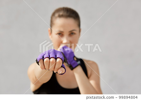 Woman preparing for workout at sport studio. Female in sportswear and fitness gloves standing isolated over gray studio background, looking directly at camera, has workout. People and sport concept. 99894804