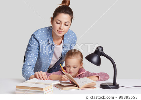Photo of mother and daugher pose at desktop together, wrtite information in notebook, read many books, prepare for lessons at school, involved in studying, isolated over white studio background 99895555