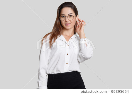 Image of pleasant looking female designer dressed in black and white clothes, big round glasses, ready to present her ideas for colleagues, isolated over white background. Woman director poses indoor Image of pleasant looking female designer dressed in black and white clothes, big round glasses, ready to present her ideas for colleagues, isolated over white background. Woman director poses indoor 99895664