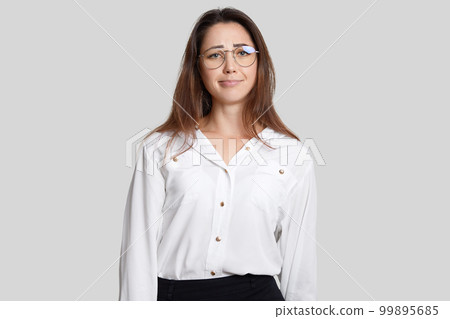 Horizontal shot of displeased European woman with dark hair, wears transparent glasses, formal clothes, looks in discontent, recieves much tasks from employer, isolated over white background Horizontal shot of displeased European woman with dark hair, wears transparent glasses, formal clothes, looks in discontent, recieves much tasks from employer, isolated over white background 99895685