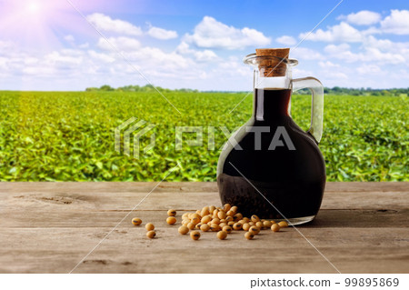 soy sauce in glass bottle with soybeans on wooden table and green agriculture field 99895869