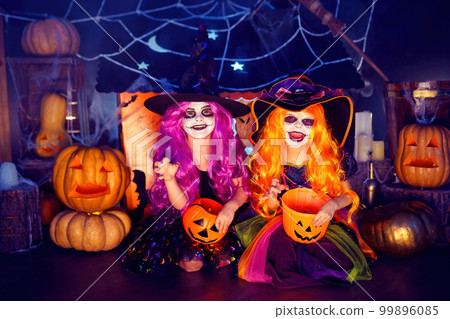 Two kid girls in witches carnival costume scaring and making faces on background decor Halloween. 99896085