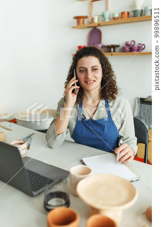 Potter entrepreneur using laptop in workshop, smiling Potter entrepreneur using laptop in workshop, smiling 99896511