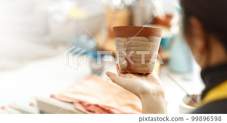 Concentrated woman painting clay jug with colourful paint shaping and sculpturing earthenware cup in pottery studio on ceramic workshop. Banner, copy space 99896598