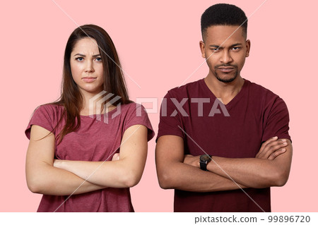 Horizontal shot of sullen displeased interracial friends keep arms folded over chest, have bad relationships, wear casual clothes, isolated over pink studio background. Negative feelings concept 99896720