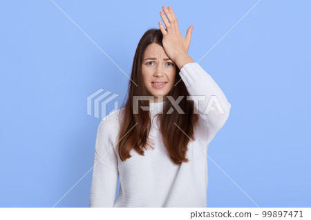 Frustrated forgetful young woman looking at camera with worried expression, holding palm on head, female realizes she forgot something important, posing isolated over blue background. Frustrated forgetful young woman looking at camera with worried expression, holding palm on head, female realizes she forgot something important, posing isolated over blue background. 99897471