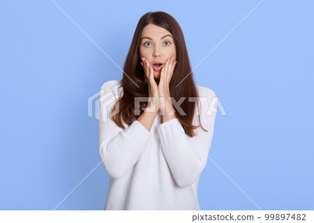 Astonished Caucasian woman cannot believe in shocking news, touches cheeks with palms, keeps mouth opened, being in great surprisement, dressed in white casual sweater, expresses fear and bewilderment Astonished Caucasian woman cannot believe in shocking news, touches cheeks with palms, keeps mouth opened, being in great surprisement, dressed in white casual sweater, expresses fear and bewilderment 99897482