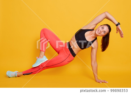 Close portrait of sporty young woman doing sport exercises isolated over yellow background, wearing stylish sportwear. Concept of healthy life and natural balance between body and mental development. 99898353