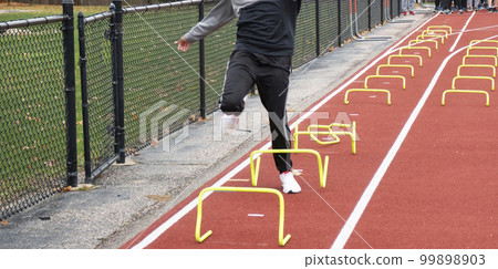 Runner tripping over yellow mini hurdles in lane on a track 99898903