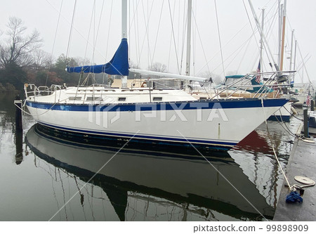 Sailboat moored in boat slip with reflection in still water on a foggy winter morning 99898909