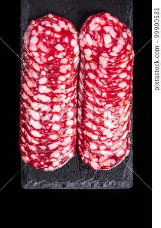 Sliced salami on a slate serving Board. Black isolated background. Top view Sliced salami on a slate serving Board. Black isolated background. Top view 99900581